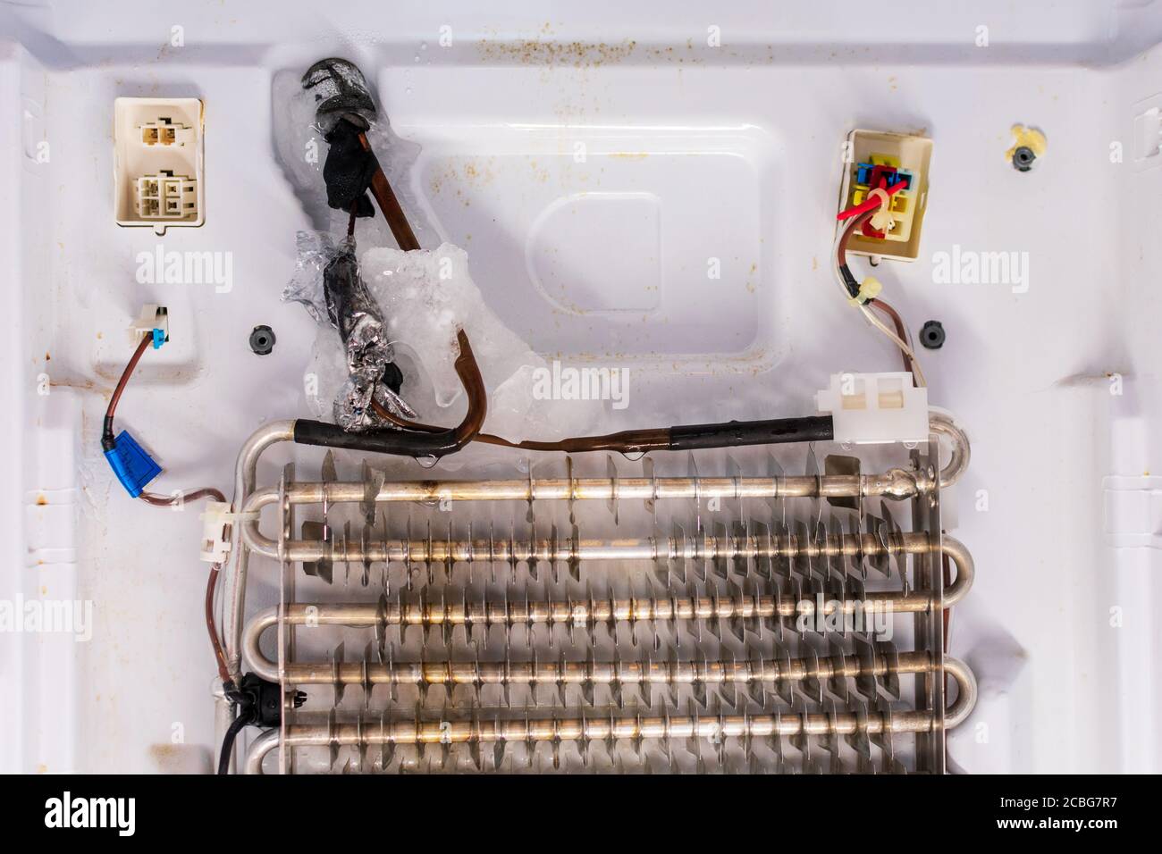 A real photo of a freezer compartment with the back interior panel removed, showing an evaporator coil covered in thick white frost