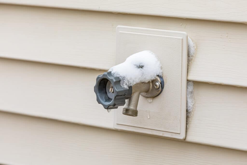 A real photo of a frost-free outdoor faucet mounted on light-colored vinyl siding with no hose attached, early winter lighting