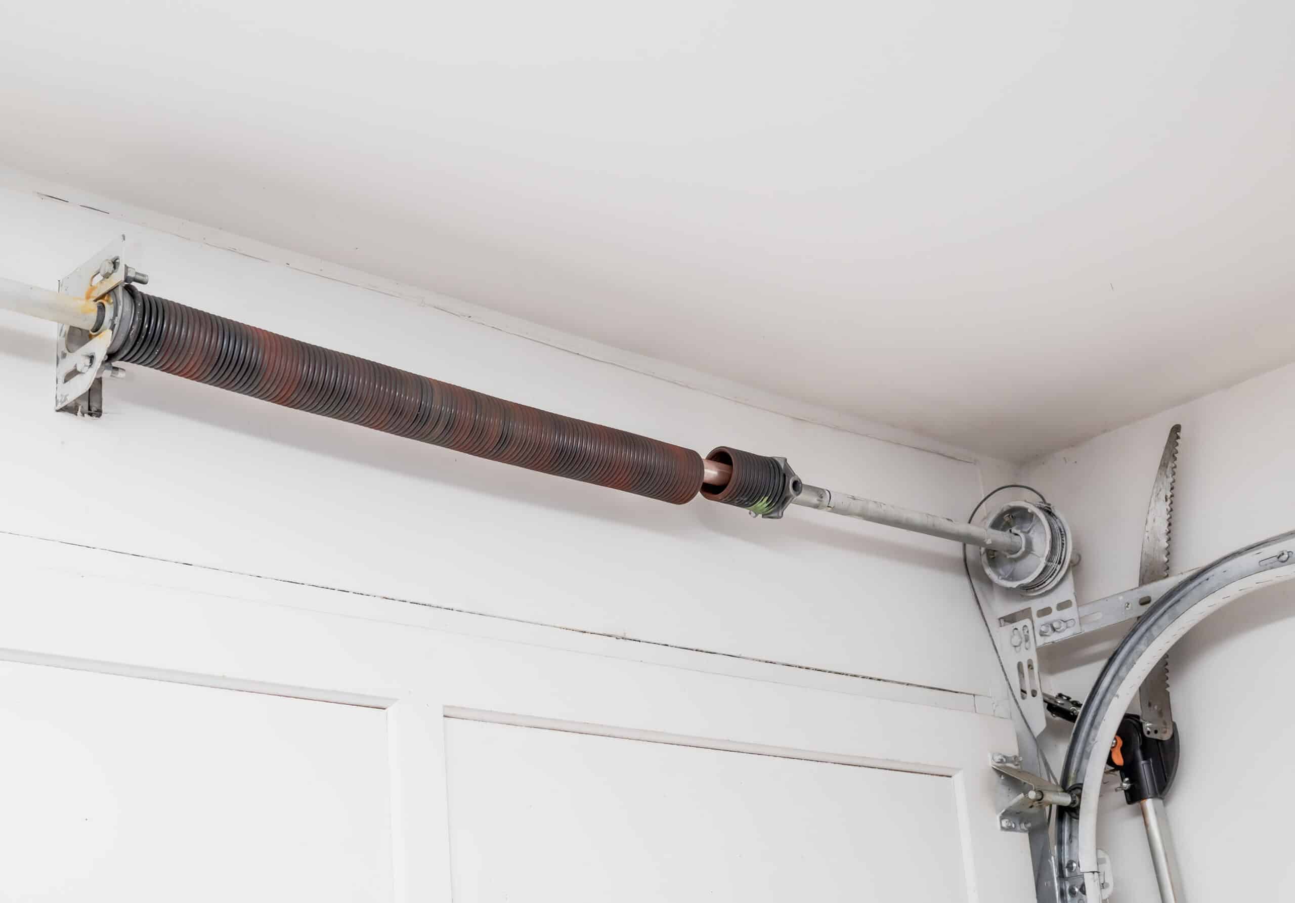 A real photo of a garage door torsion spring mounted above the door with a visible separation gap indicating a broken spring