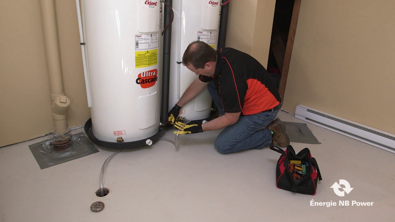 A real photo of a garden hose attached to a water heater drain valve, running across a basement floor into a floor drain