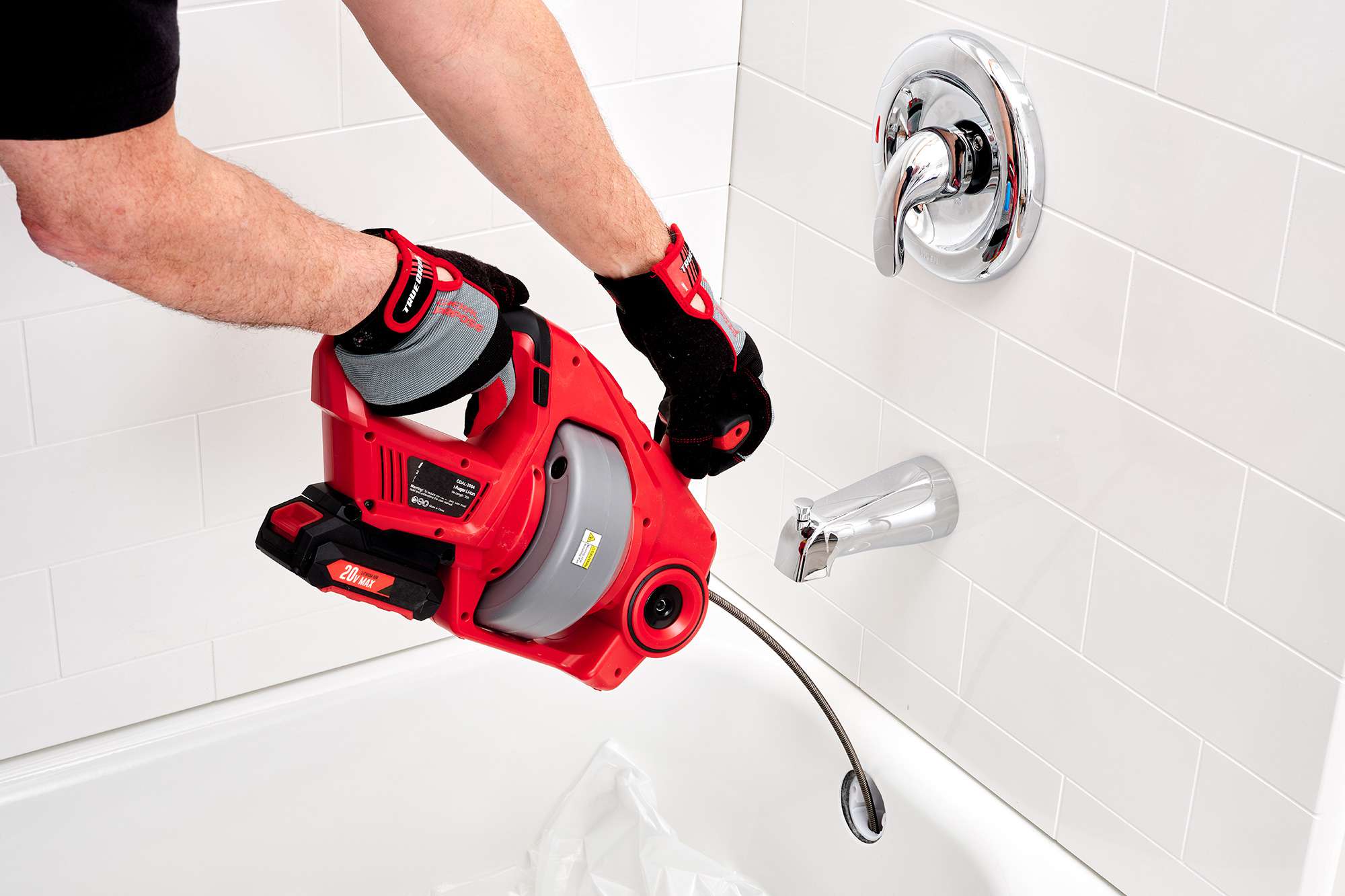A real photo of a hand auger drain snake being fed into a bathtub drain with the stopper removed