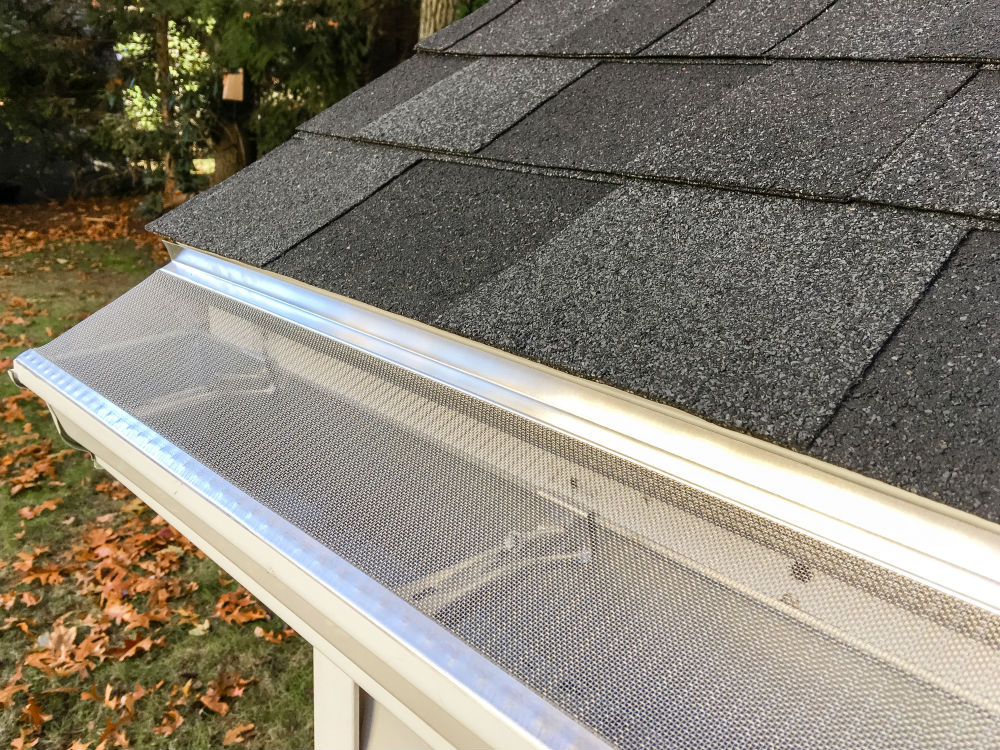 A real photo of a micro-mesh gutter guard installed along an asphalt shingle roof edge on a suburban home