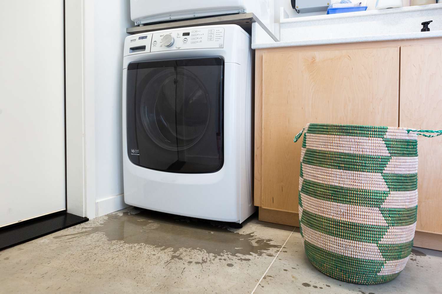 A real photo of a modern washing machine in a laundry room with a small puddle of water on the tile floor in front of it, natural indoor light, realistic home setting