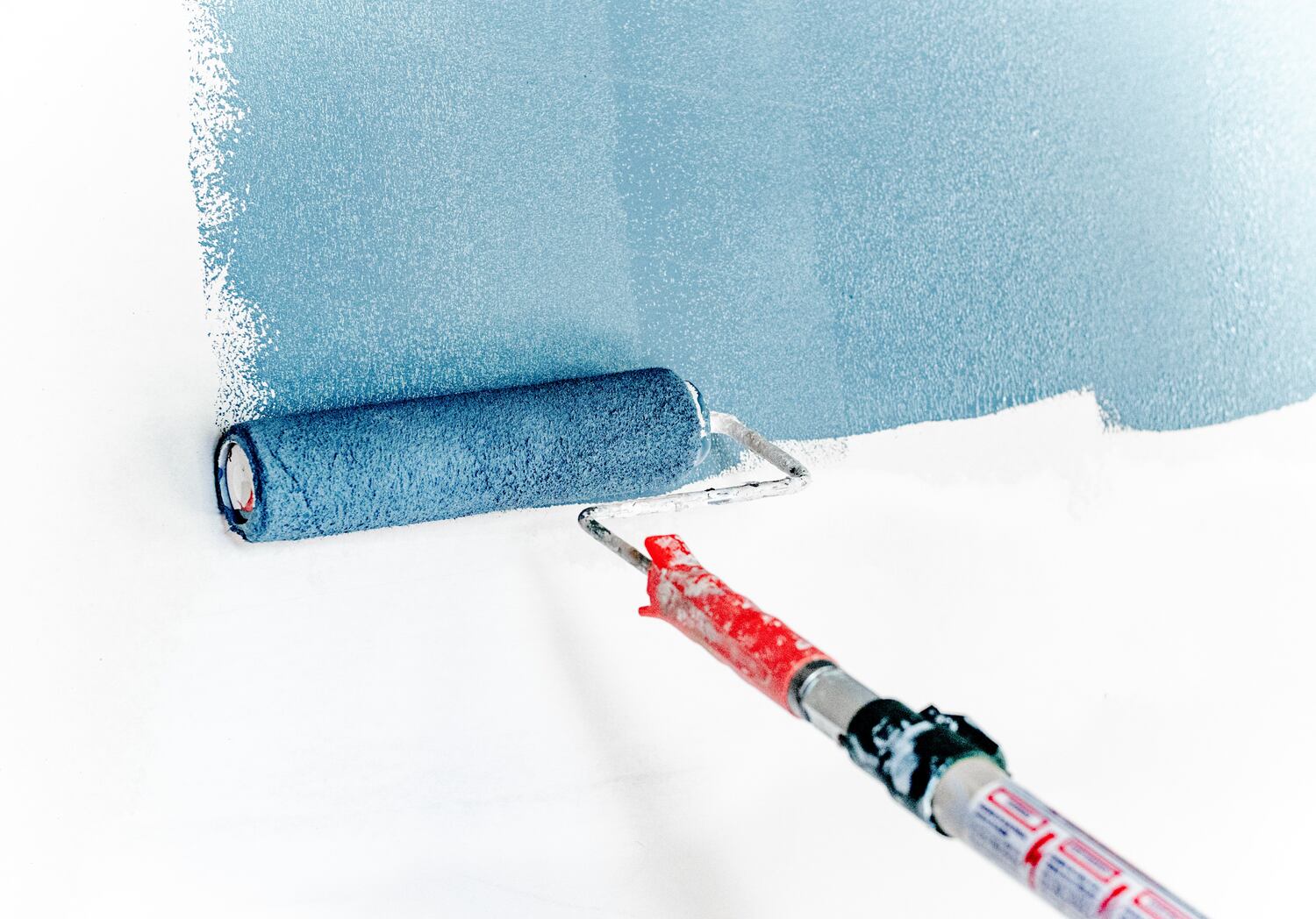 A real photo of a person using a small paint roller to repaint a freshly primed drywall patch on a white ceiling, indoor home improvement scene
