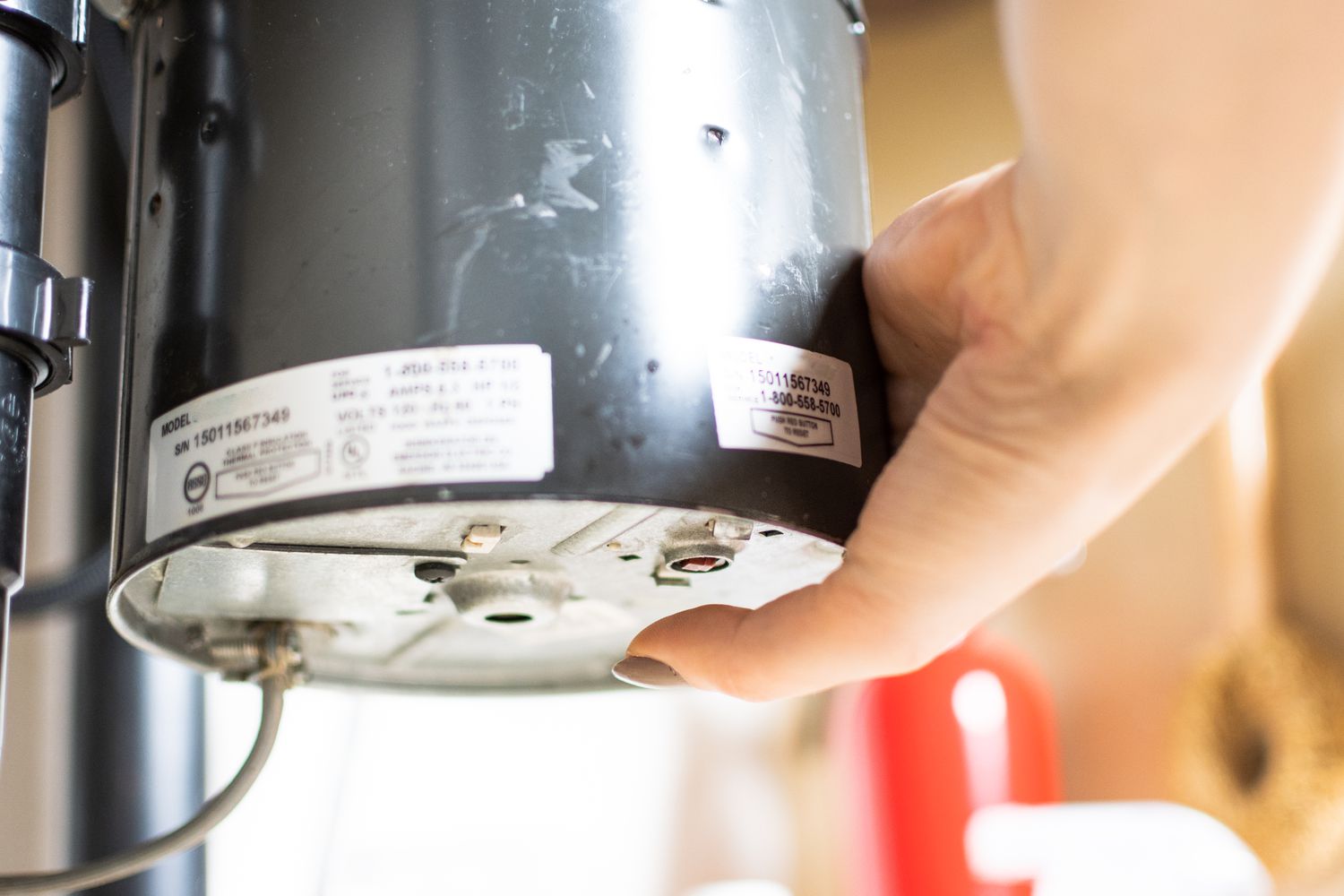 A real photo of a person using an Allen wrench on the underside socket of a garbage disposal to free a jam