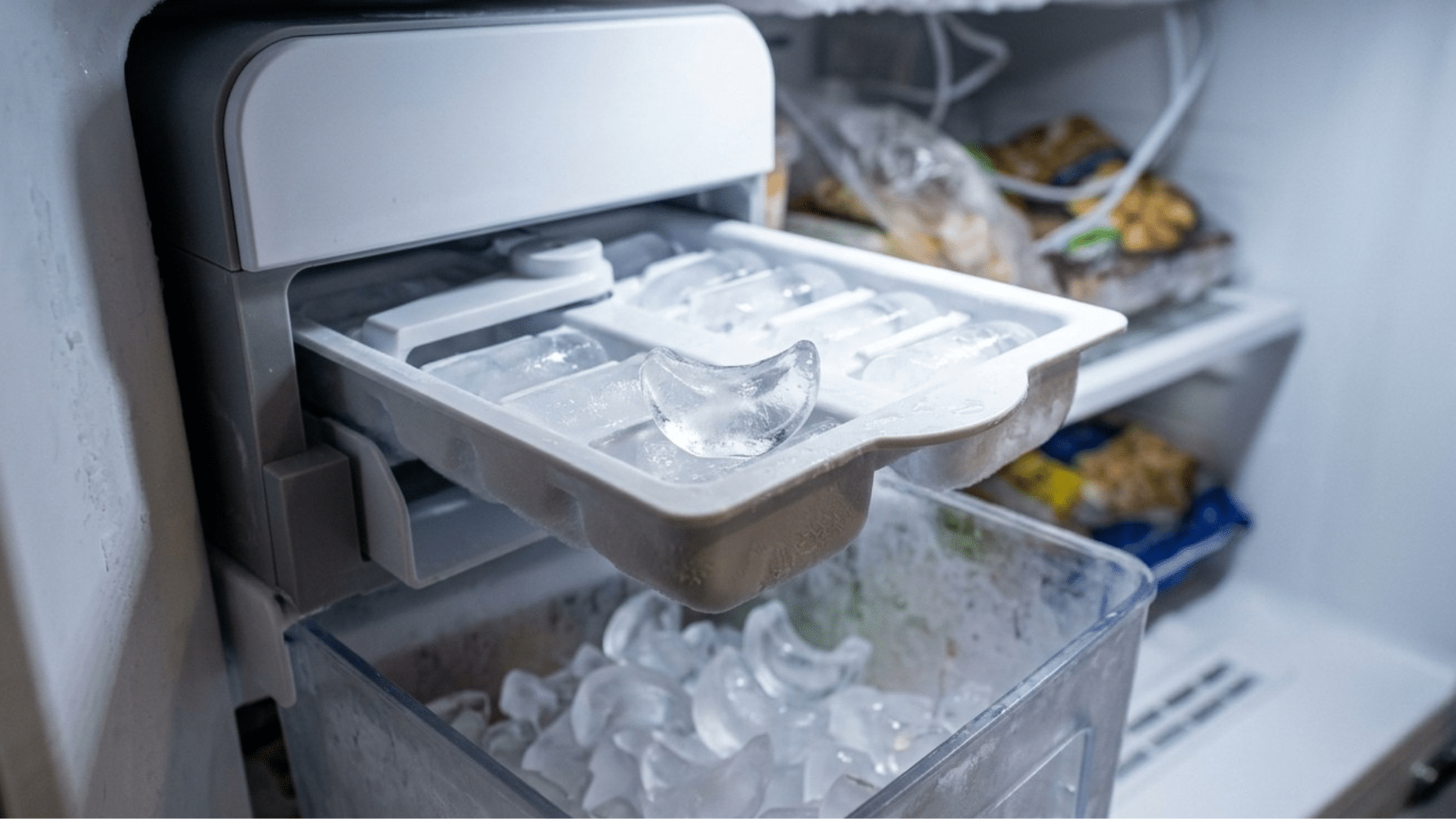 A real photo of a refrigerator freezer interior with an ice maker mounted on the side wall above an ice bin, with the ice mold visible