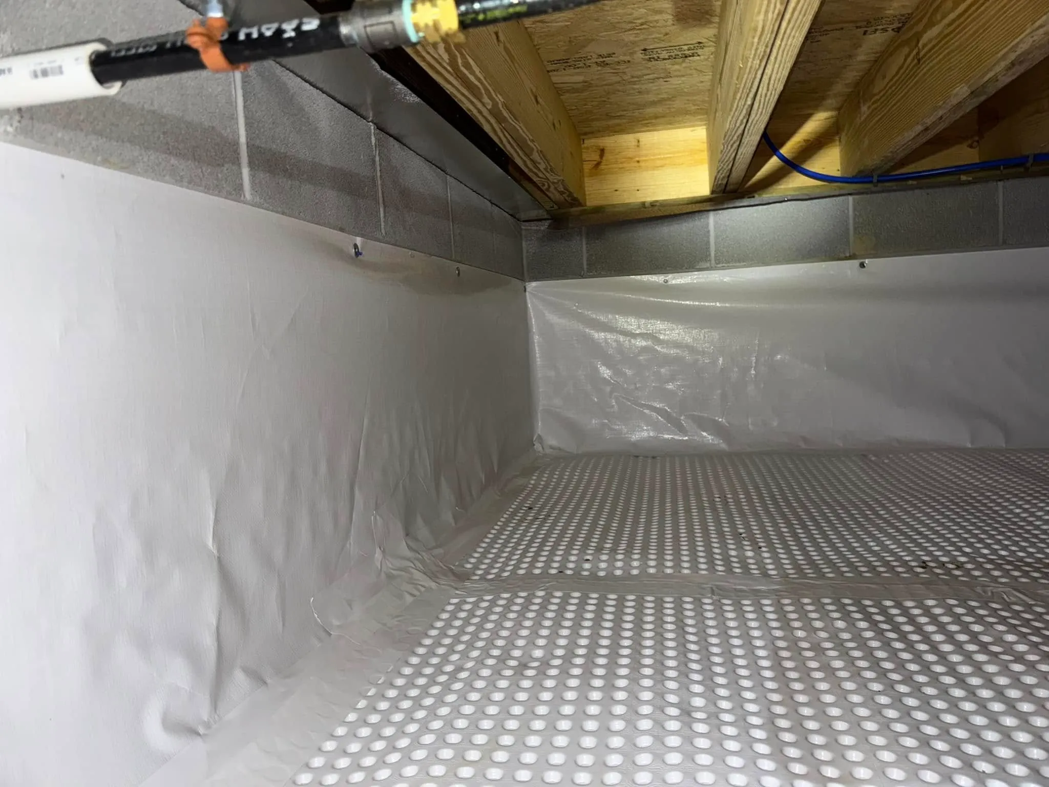 A real photo of a residential crawl space after encapsulation, showing a clean white sealed liner covering the floor and foundation walls with sealed seams