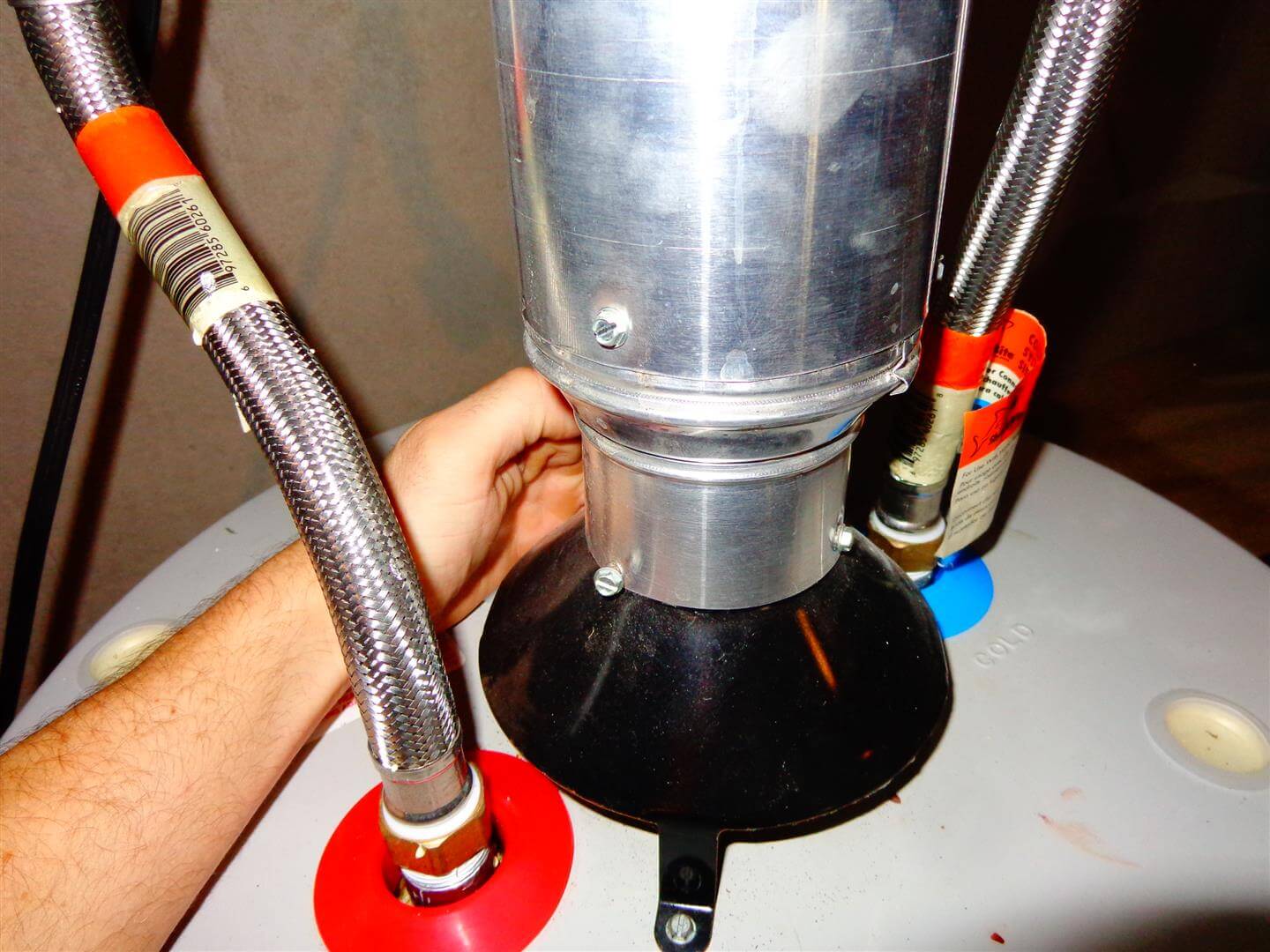 A real photo of a residential gas tank water heater in a utility room with the metal vent pipe and draft hood visible above the tank