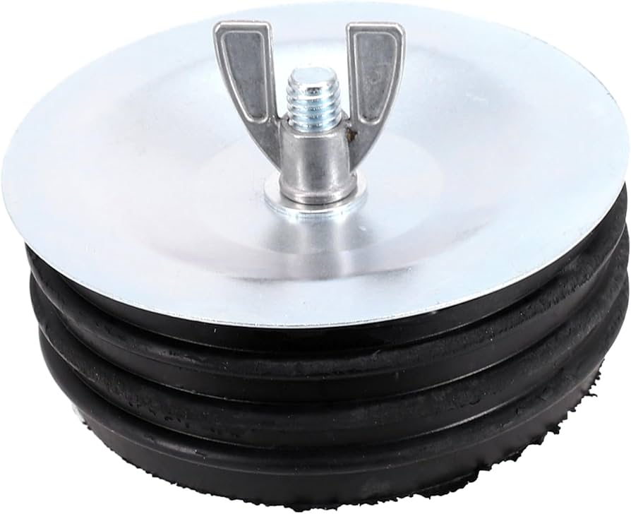 A real photo of a sewer cleanout cap held in a gloved hand showing a flattened, dirty rubber gasket on the underside, with the cleanout pipe blurred in the background