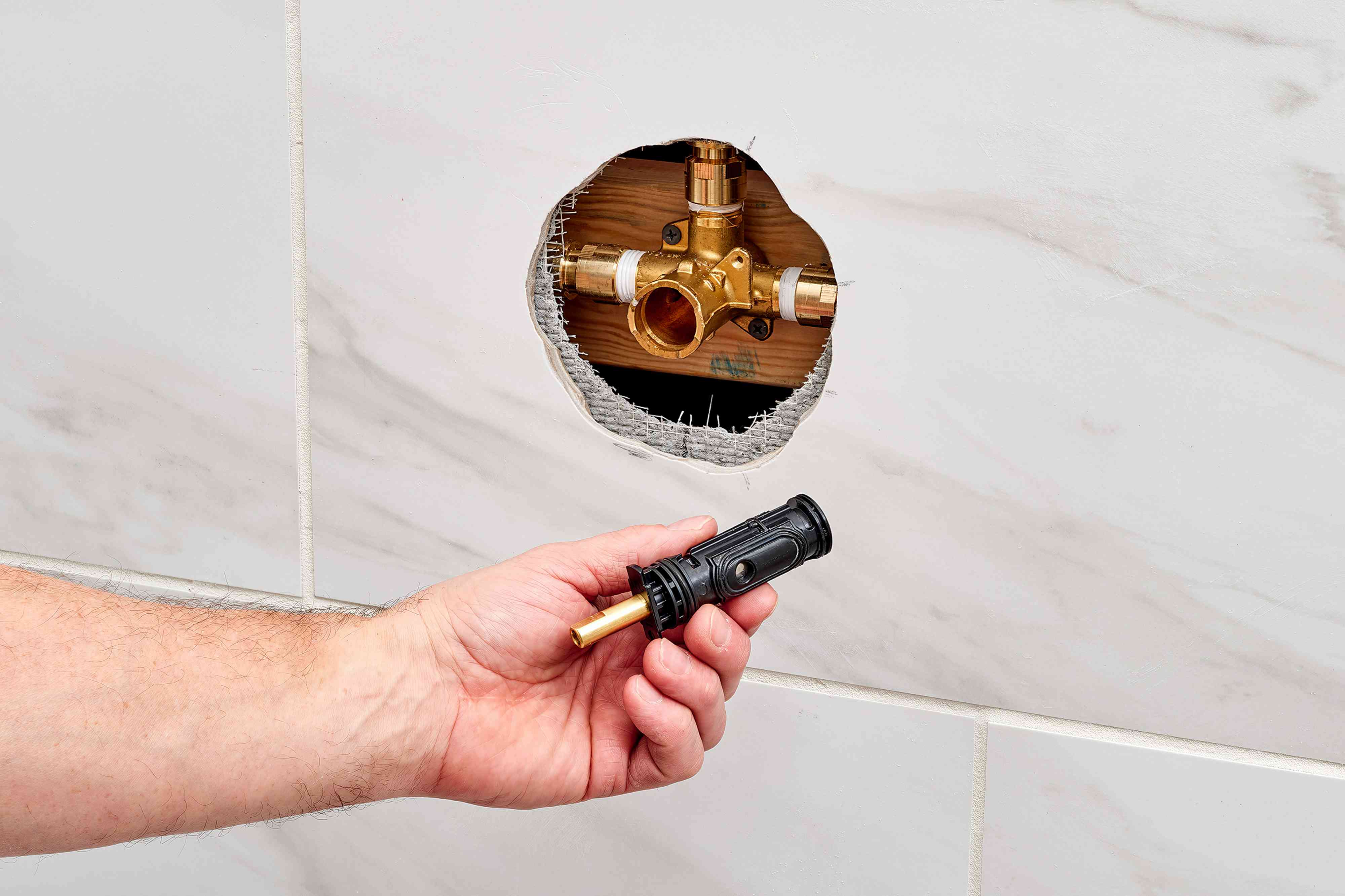 A real photo of a single-handle shower control with the trim plate removed, exposing the valve body and cartridge area in a bathroom wall