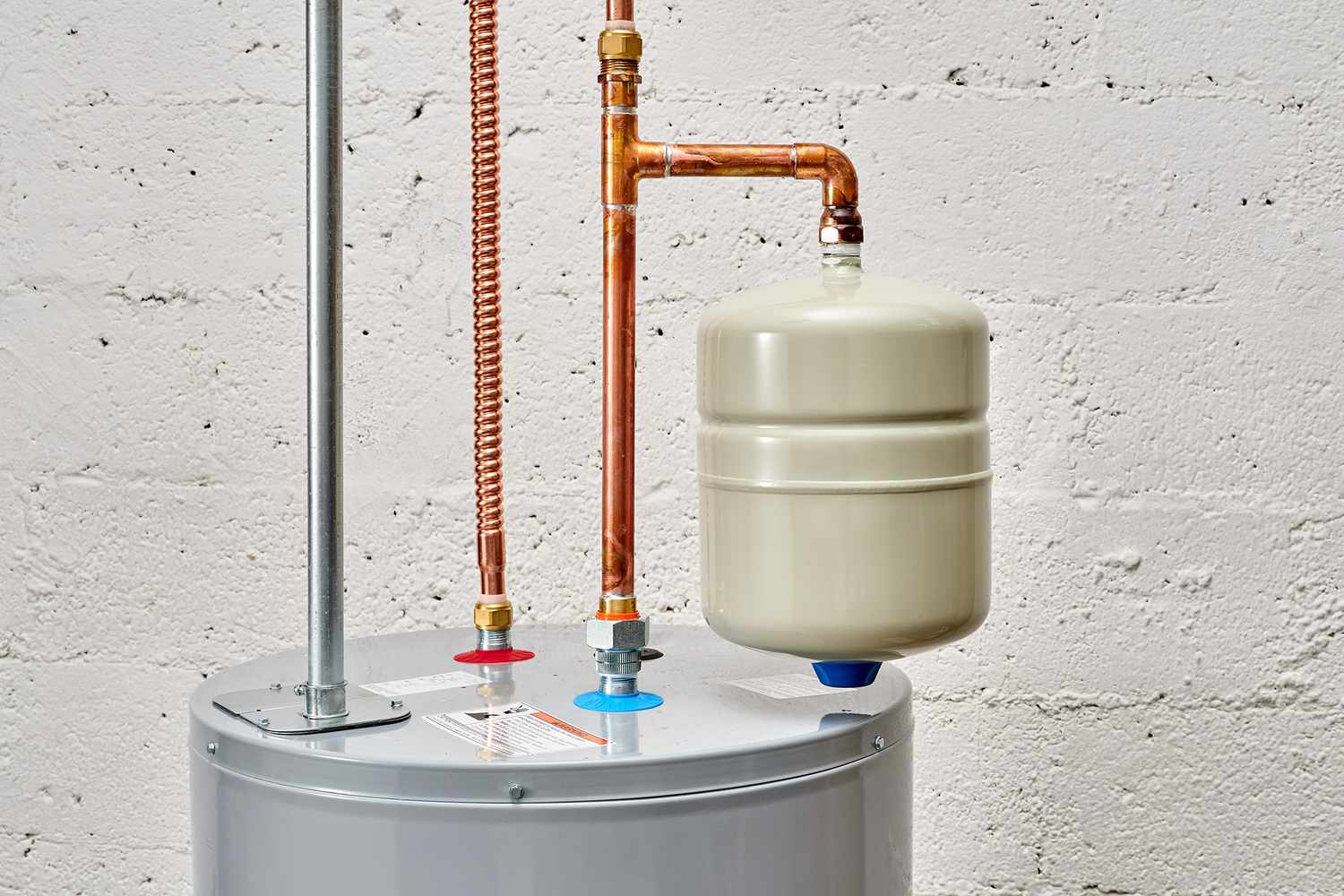 A real photo of a small thermal expansion tank mounted above a residential water heater on copper piping in a utility room