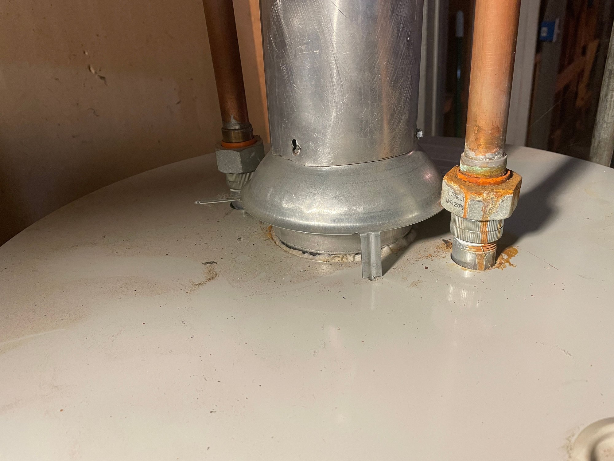 A real photo of an older electric water heater with the access panel removed showing rust and corrosion around the opening, garage utility room setting