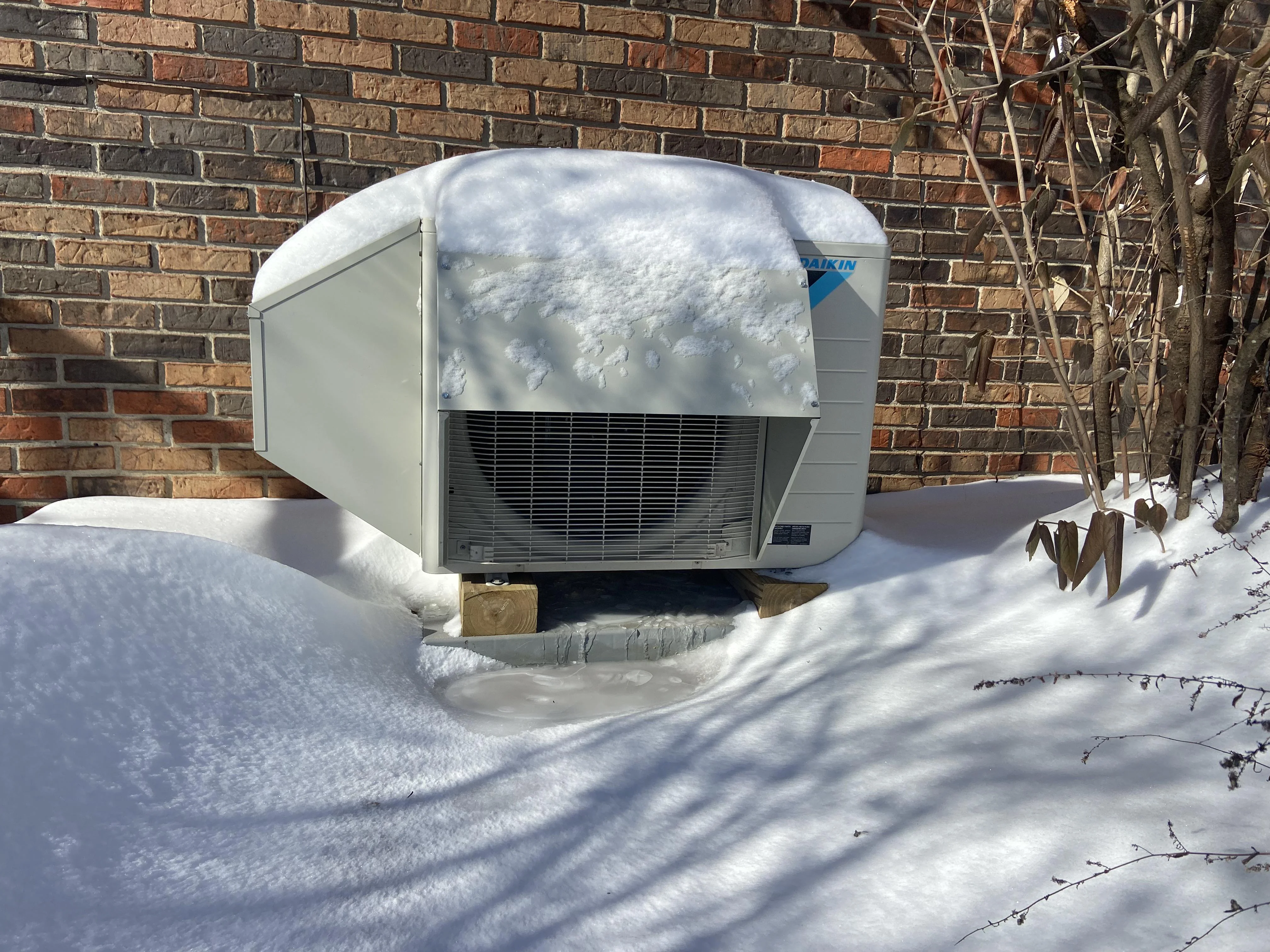 A real photo of an outdoor heat pump condenser running on a cold morning with light frost on the coil and a clear area around the unit