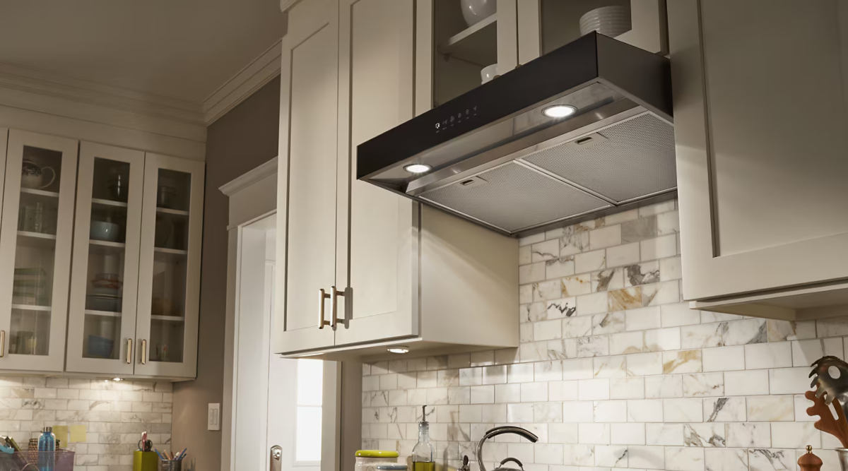 A real photo of an under-cabinet range hood power cord plugged into a duplex outlet inside an upper cabinet above a stove