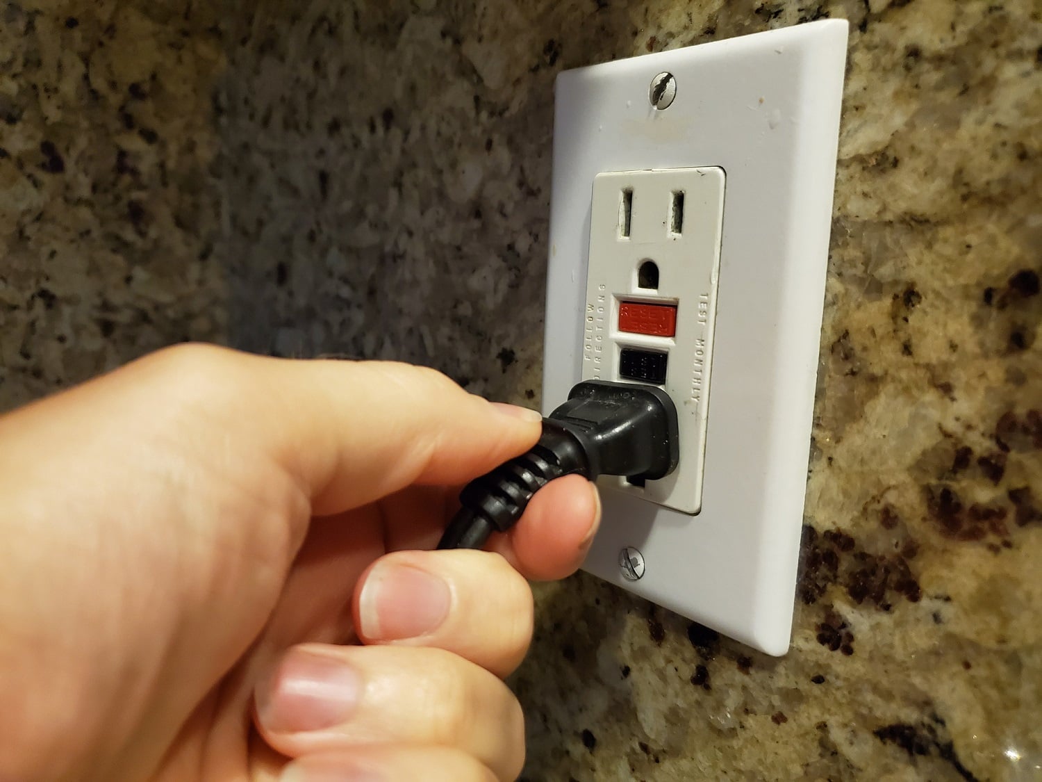 A real photo of hands using a screwdriver to install a new GFCI outlet into an electrical box, with wires visible and the breaker off