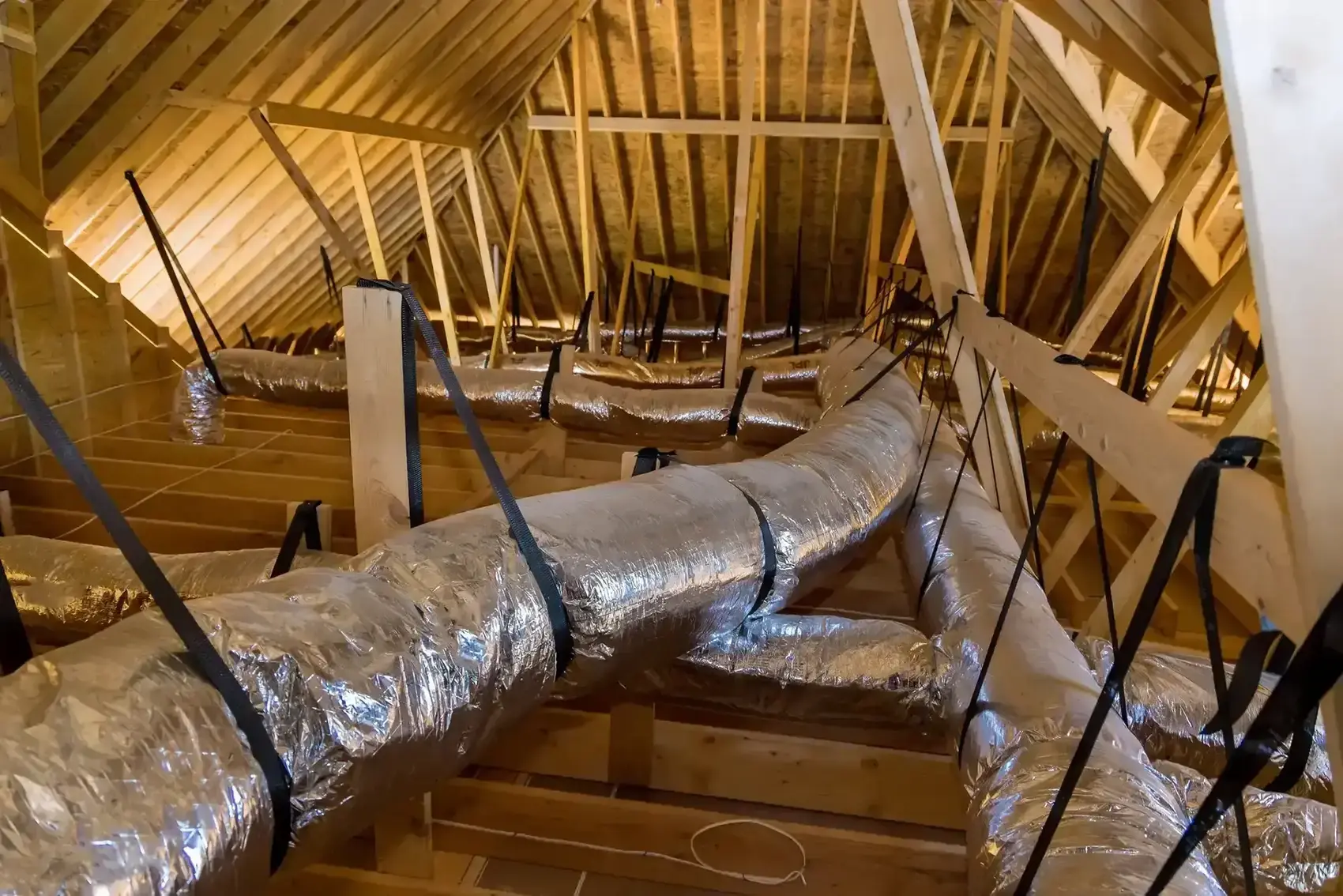 A real photo of insulated flexible HVAC ductwork connected to a metal collar in a home attic with visible straps and framing