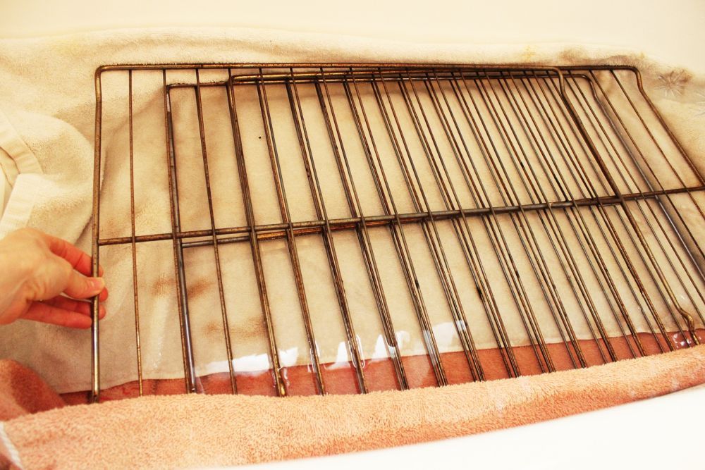 A real photo of oven racks soaking in a bathtub filled with hot soapy water, no text or labels