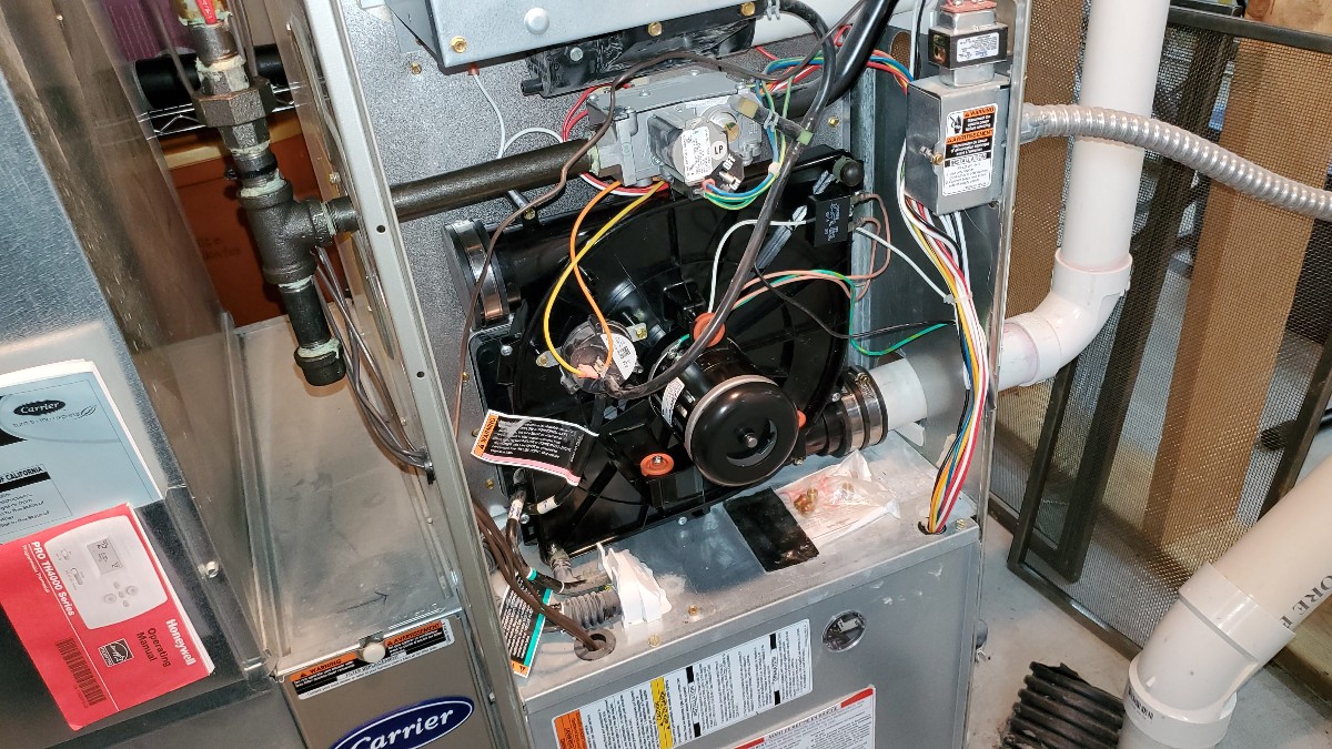 A real photo of the inside of a residential gas furnace showing the draft inducer motor mounted near the flue connection, with wiring and vent pipe visible