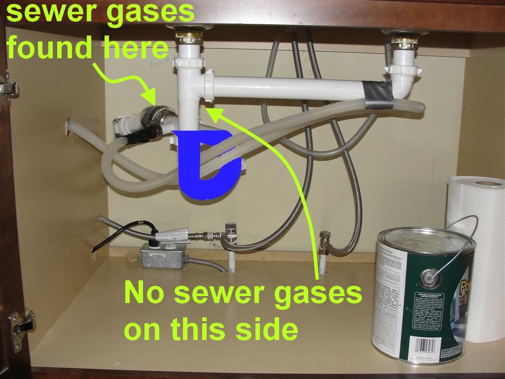 A real photo under a kitchen sink showing a dishwasher drain hose clamped to a garbage disposal dishwasher inlet with the hose routed up high first