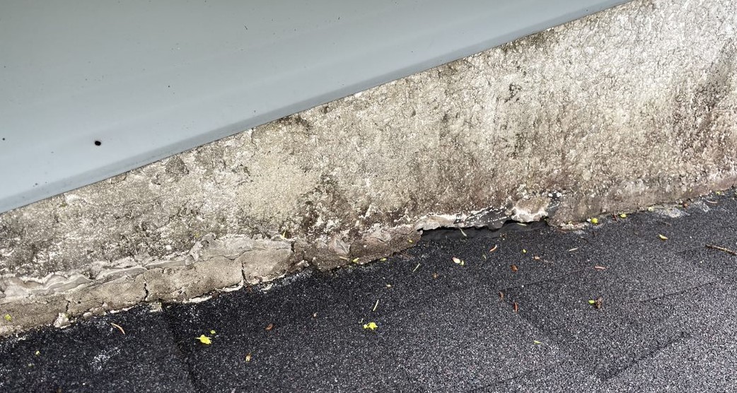 A real photograph of a homeowner applying exterior-grade caulk around a utility line penetration on house siding on a sunny day, close-up of hands and caulk gun