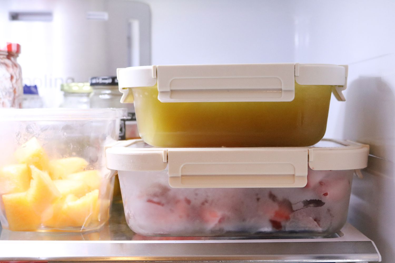 A real refrigerator shelf with large food containers pushed against the back wall, visibly blocking the airflow vent area, indoor kitchen photo