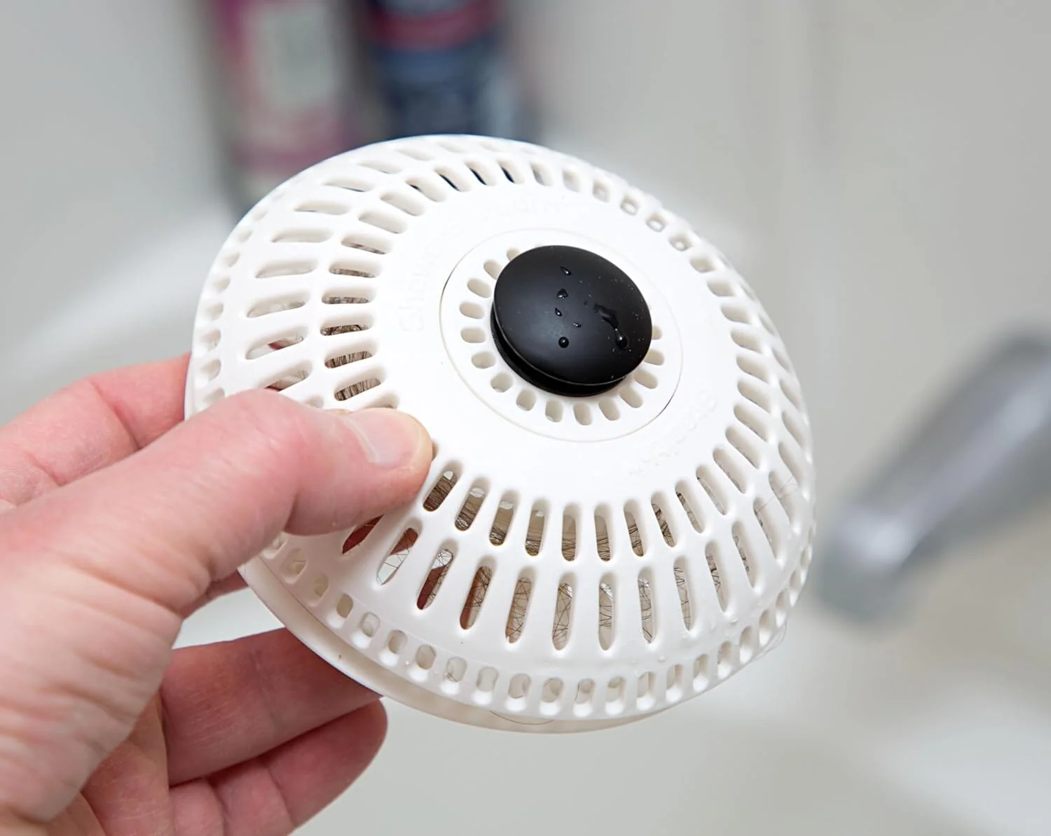 A real shower floor drain with a silicone hair catcher on top collecting wet hair after a shower