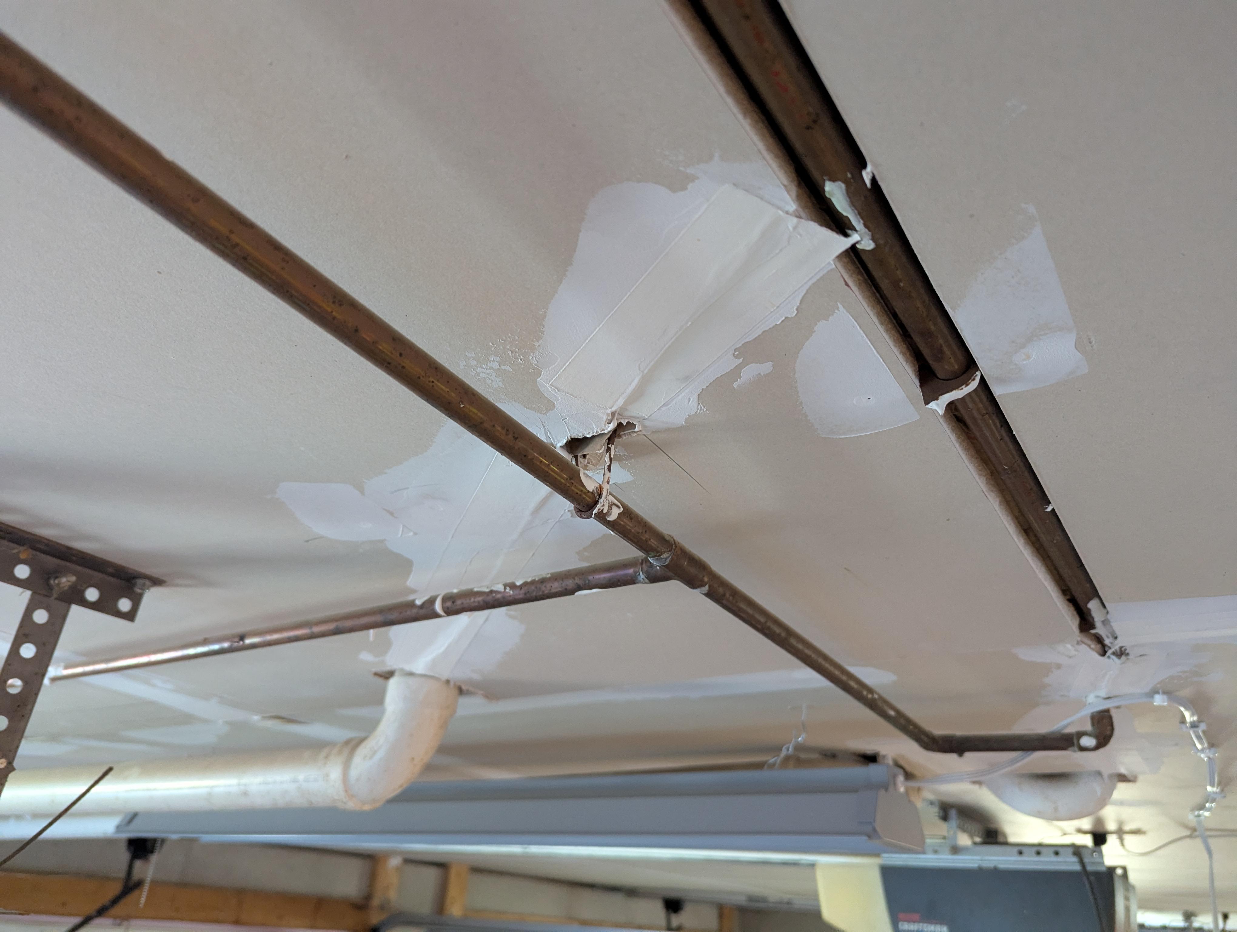 A refrigerator pulled slightly away from the wall in a cold garage, showing a thin water supply tube behind it, realistic home photo