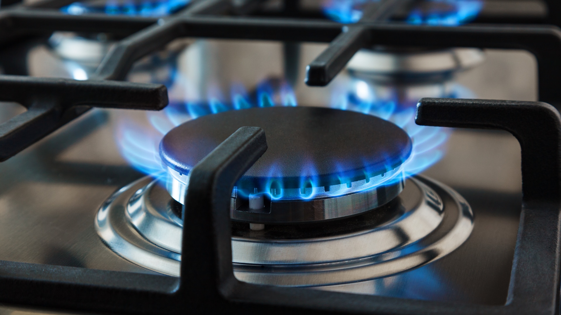 A removed gas burner head being scrubbed with a toothbrush in warm soapy water, focusing on clearing the small burner ports