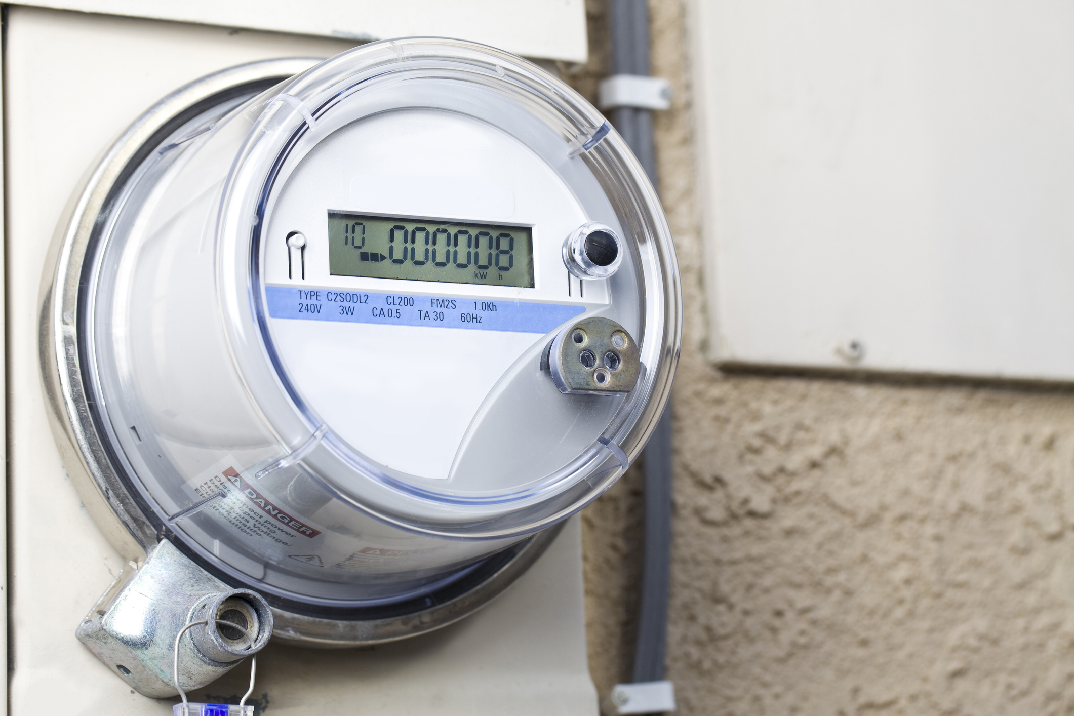 A residential electric meter mounted on an exterior wall with conduit and small gaps around penetrations where spiders could hide