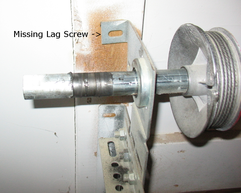 A residential garage door with a torsion spring above the door showing a visible break and gap in the coil, photographed in a real garage