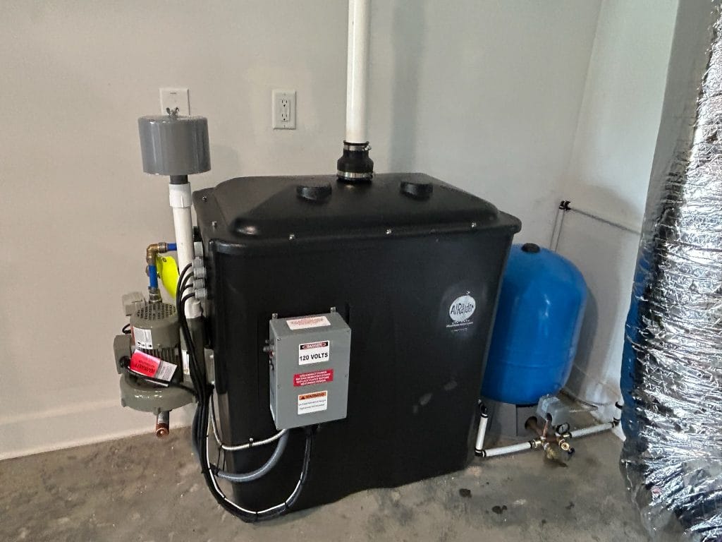 A residential well water aeration or air-injection treatment tank installed in a basement utility area with clean plumbing connections, real photo