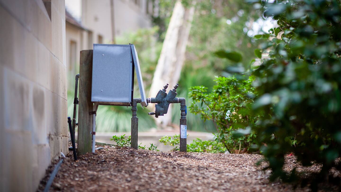 A single photo of a residential water meter box opened near a curb, showing the meter and shutoff valve inside