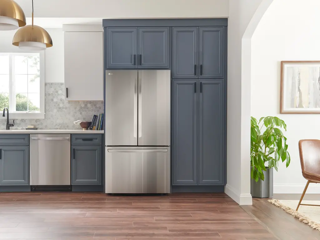 A stainless steel refrigerator water dispenser in a home kitchen with a glass being filled, natural indoor lighting, real photo