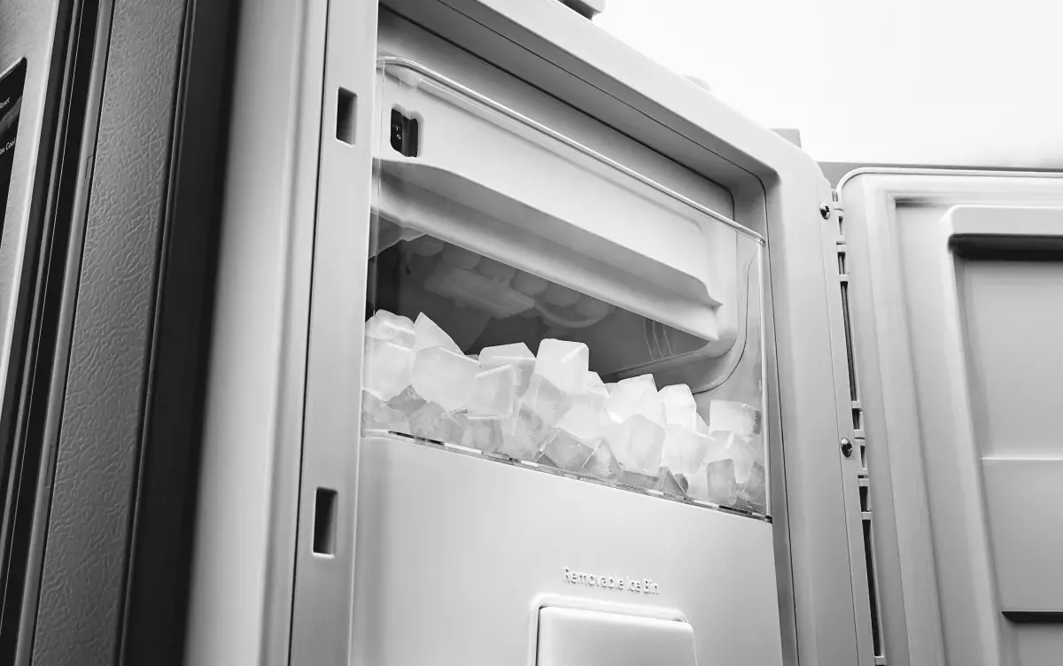 A stainless steel refrigerator with the freezer door open while a homeowner inspects the ice bin and dispenser area in a real kitchen