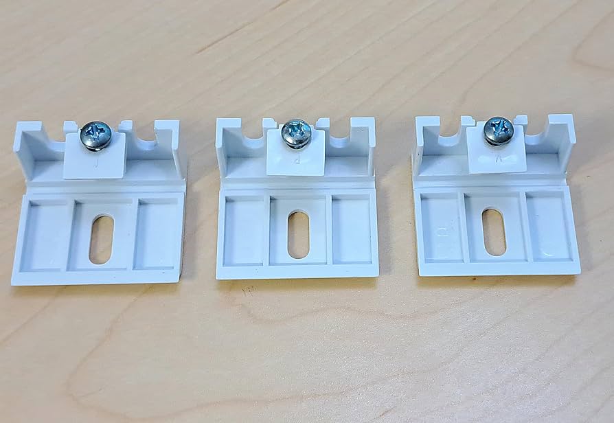 A tabletop photo of cellular shade installation parts including metal mounting brackets, small screws, and plastic end caps laid out neatly