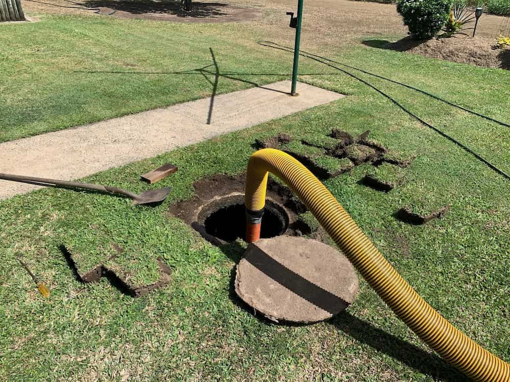 A thick vacuum hose connected to an open septic tank access lid during a routine pump-out at a home, real photo