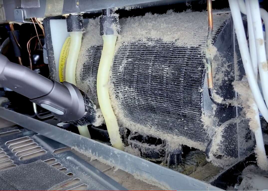 A vacuum hose cleaning dust and pet hair from the condenser coils underneath a refrigerator