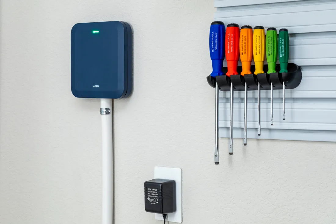 A wall-mounted lawn irrigation controller with a homeowner's hand pressing buttons to start a manual station test, indoor utility area photo