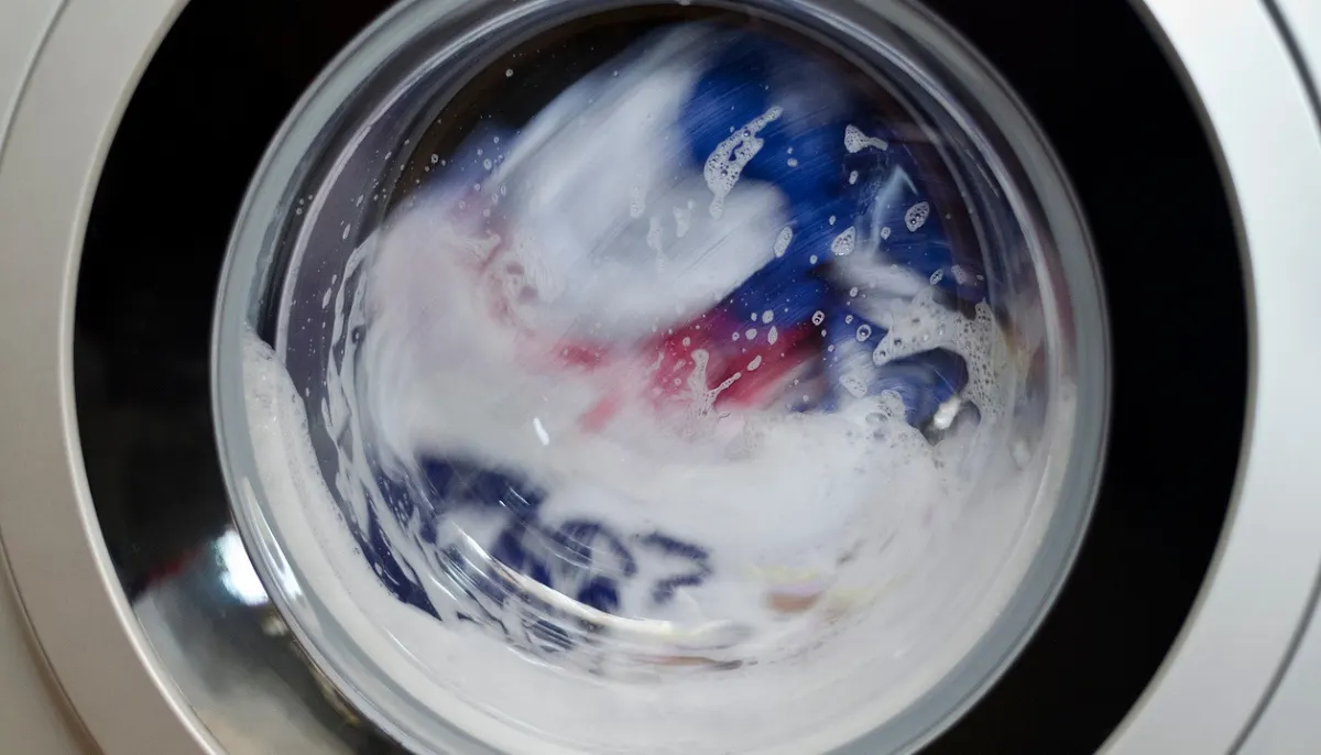 A washing machine drum filled with excessive soap suds rising above the clothes during a wash cycle