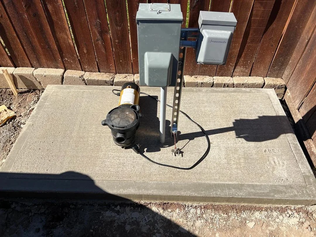 A weather-resistant outdoor GFCI outlet on a wall near pool equipment, with the reset and test buttons visible in daylight
