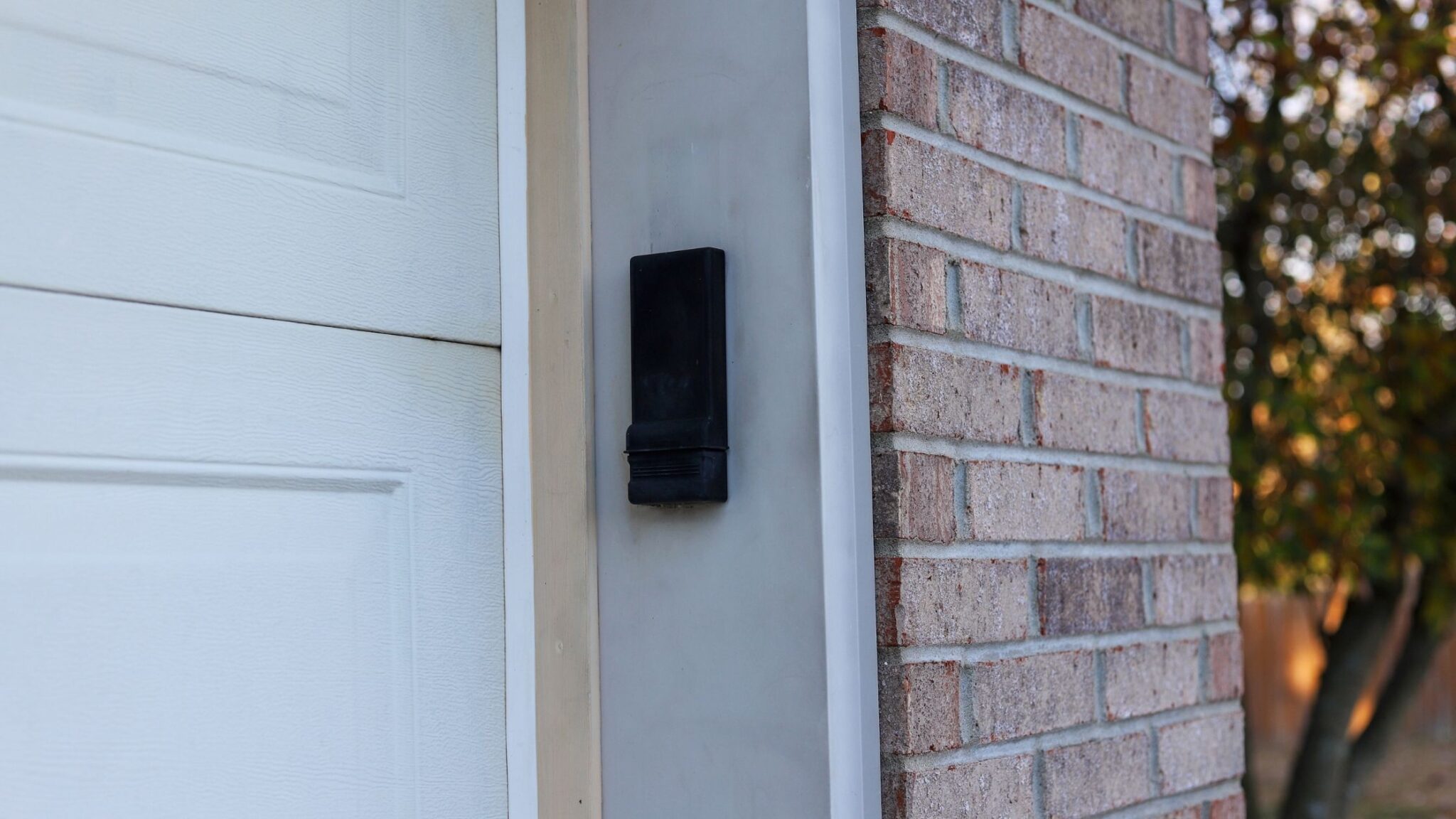 A weathered garage door keypad mounted on exterior trim beside a garage door, photographed in daylight