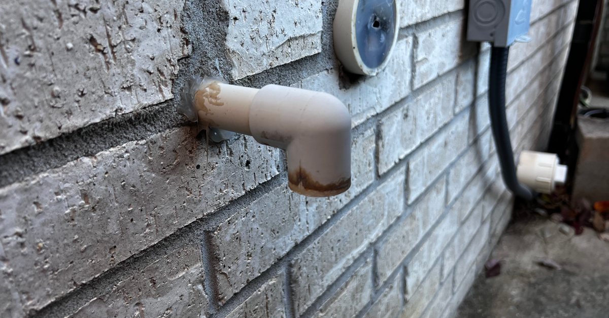 A wet dry vacuum hose attached to an outdoor HVAC condensate drain pipe, realistic home maintenance photo