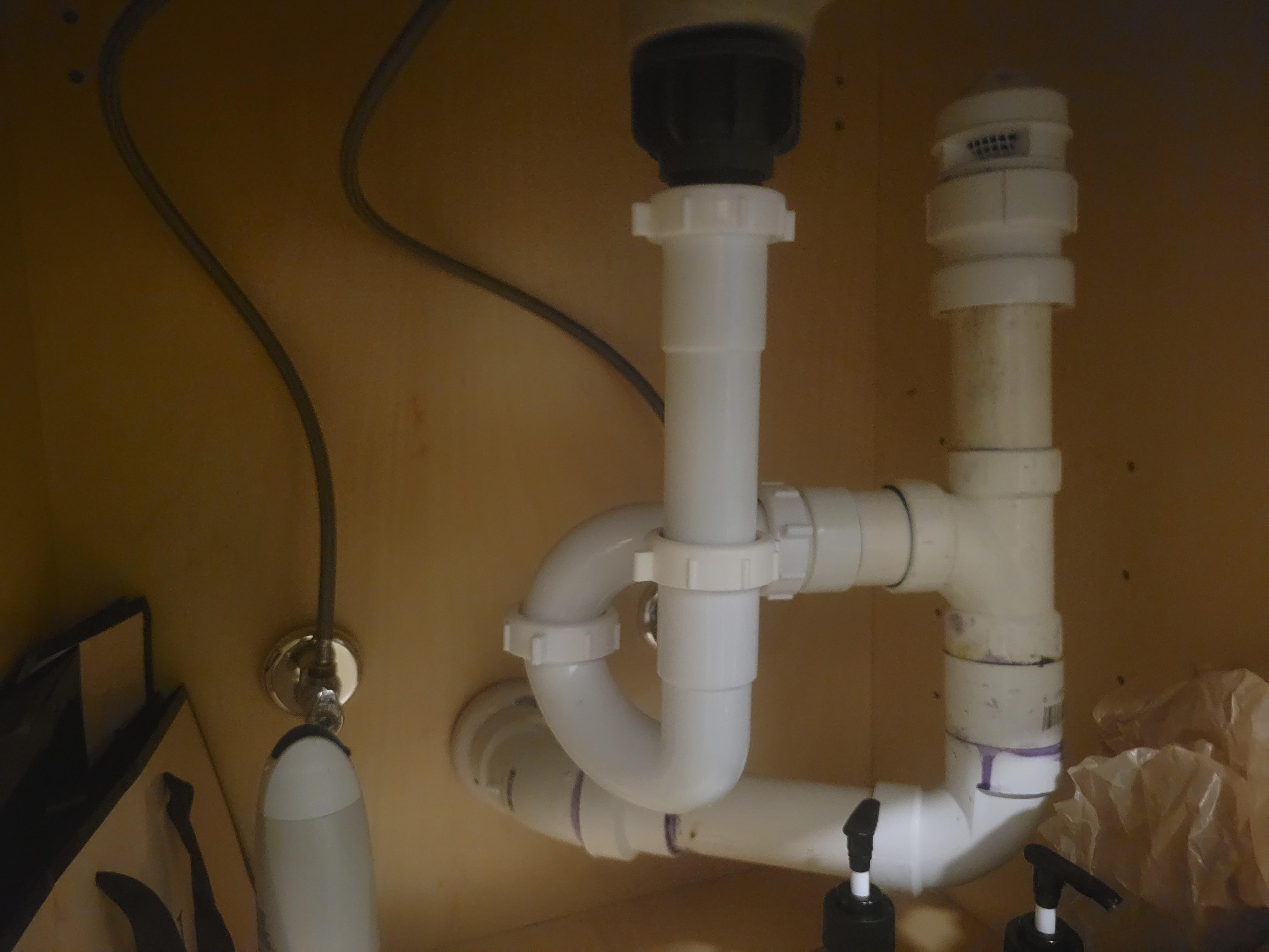 Air admittance valve installed on a vertical pipe under a kitchen sink inside the base cabinet