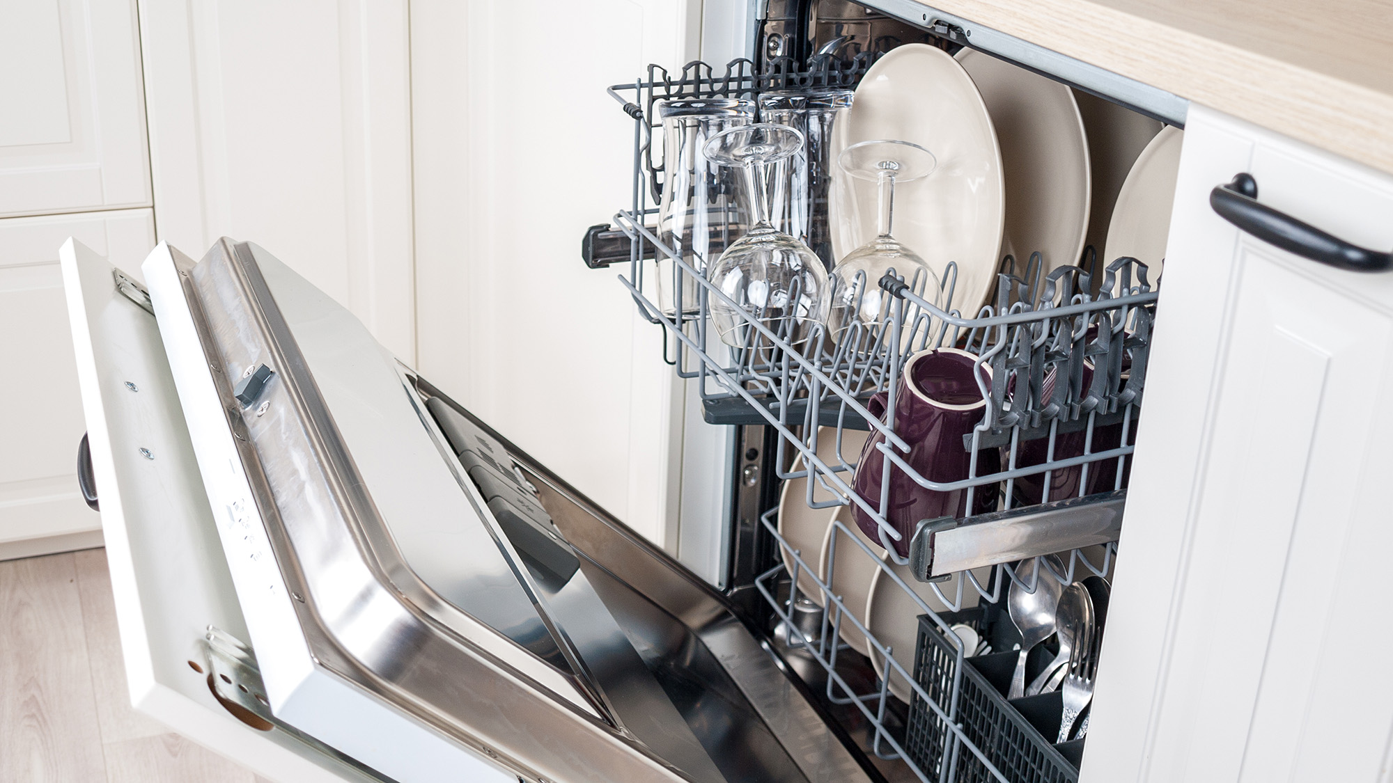 An open dishwasher with clean but wet dishes and visible water droplets on glassware, in a typical home kitchen