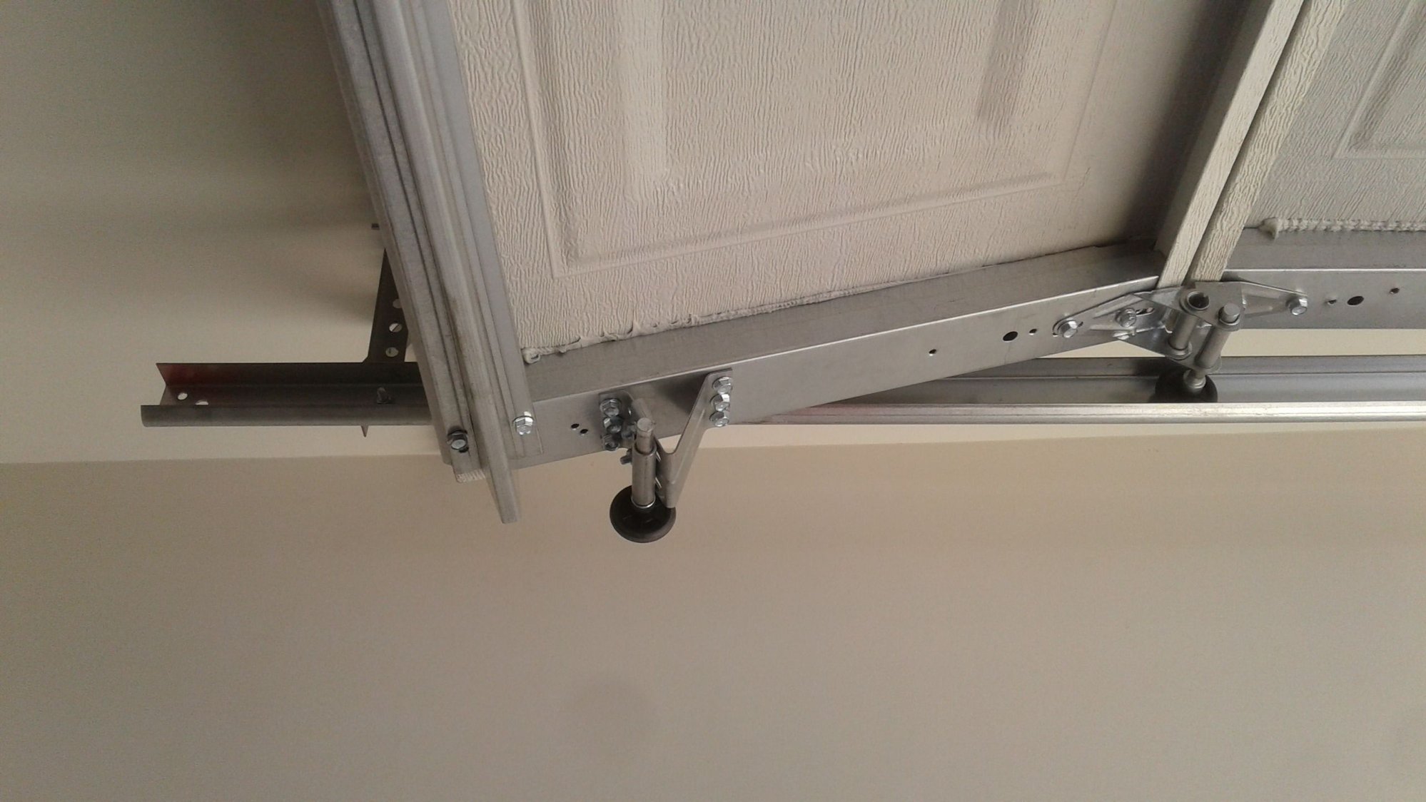 Close-up photo of a garage door roller sitting outside the curved metal track near the top corner of a sectional door