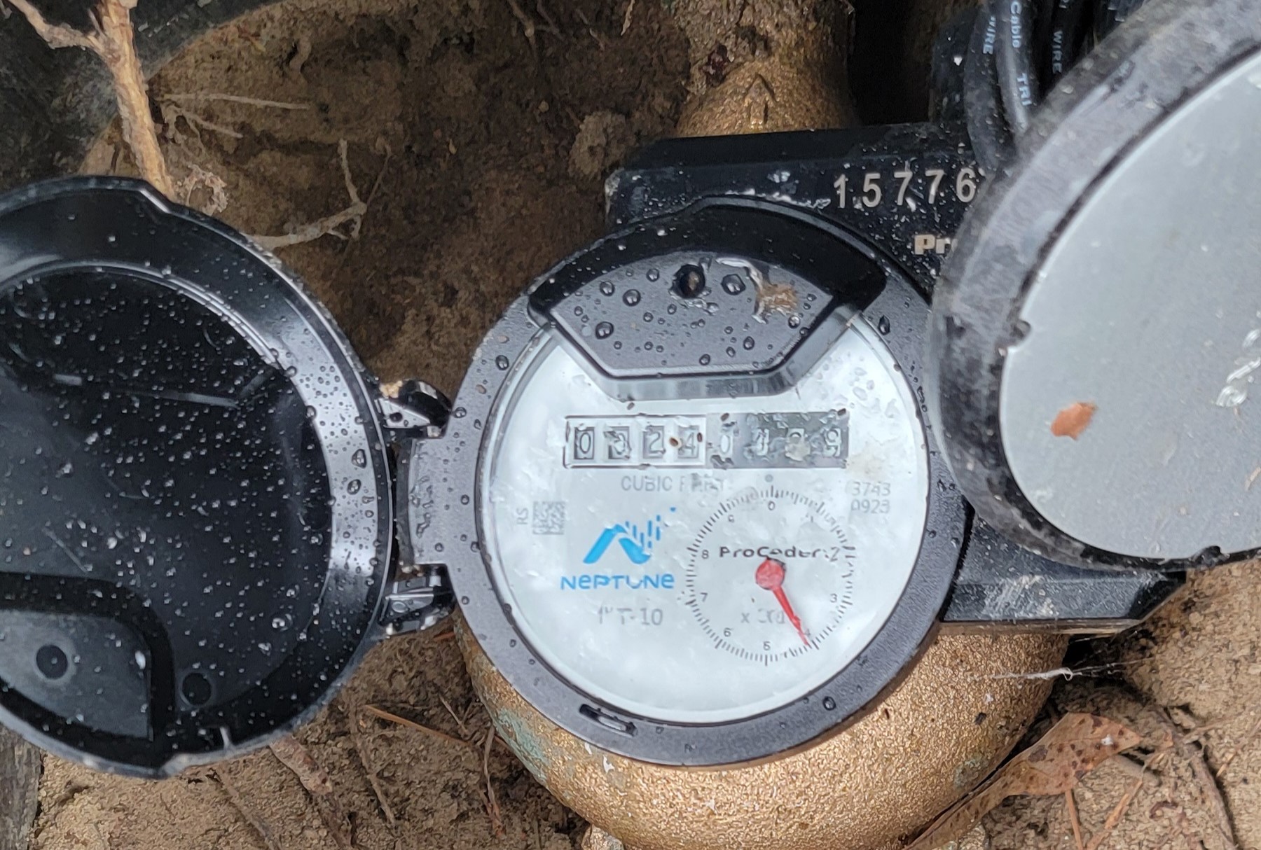 Close-up photo of a residential water meter dial with a small leak indicator visible, showing fine detail of the numbers and dial