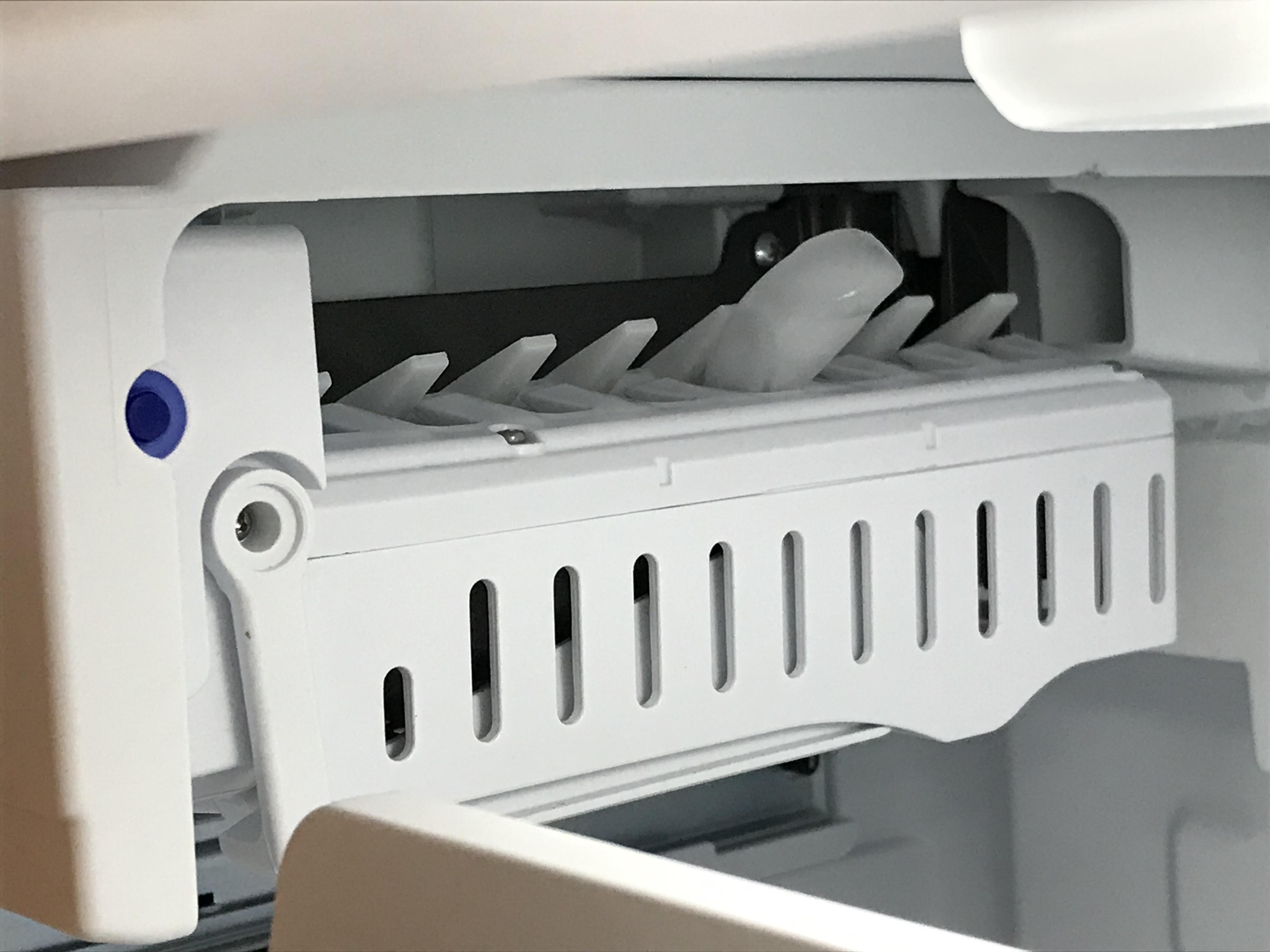 Close-up photo of an ice maker with ejector fingers partially rotated and frozen in place, with cubes wedged in the ice mold