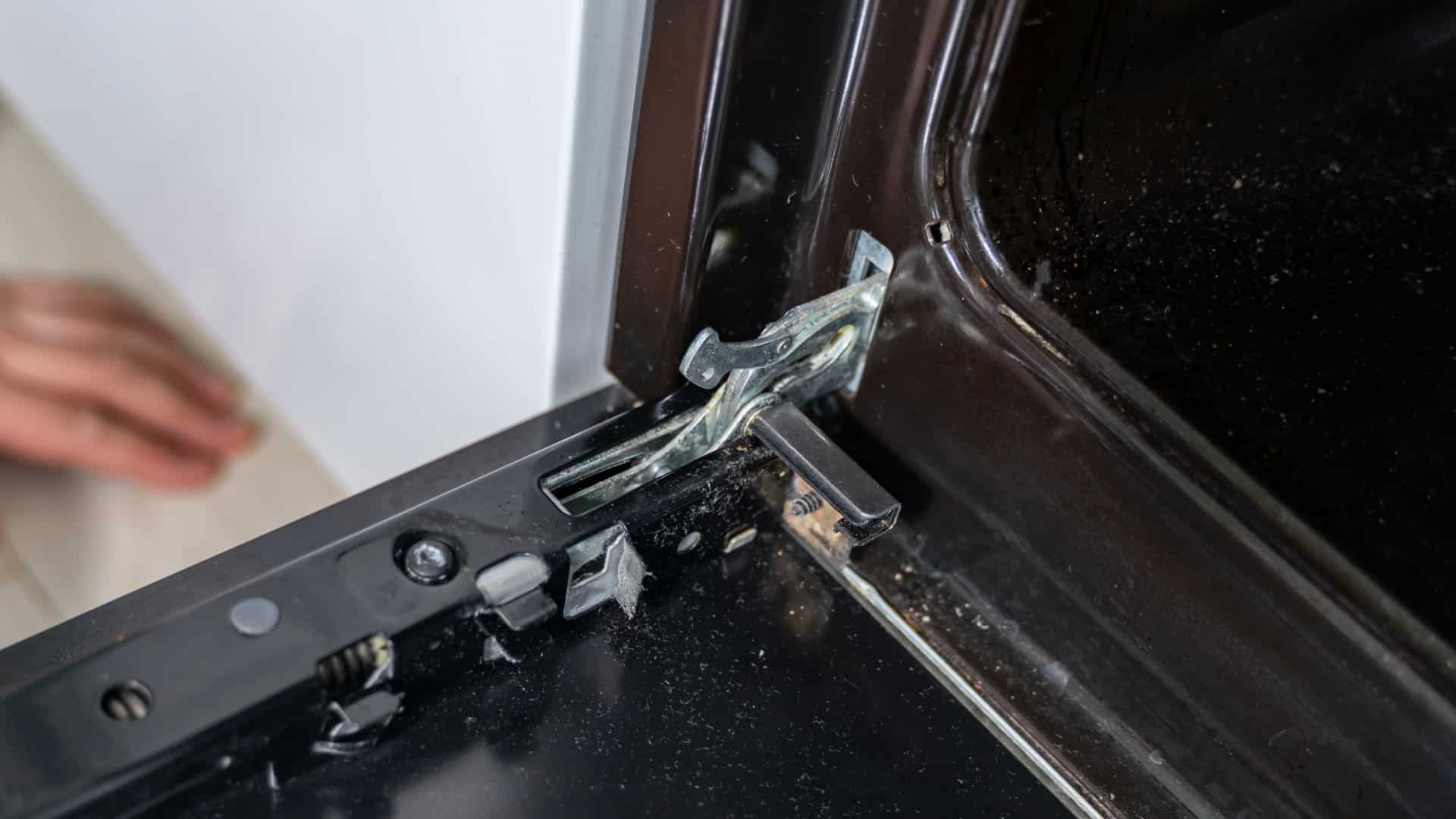 Close-up photo of an oven door hinge assembly partially extended from the oven frame, showing metal hinge arms and mounting points, workshop lighting, photorealistic