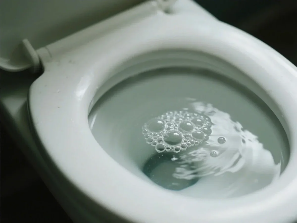 Close-up photo of clear toilet bowl water with a small cluster of bubbles collecting near the front of the bowl