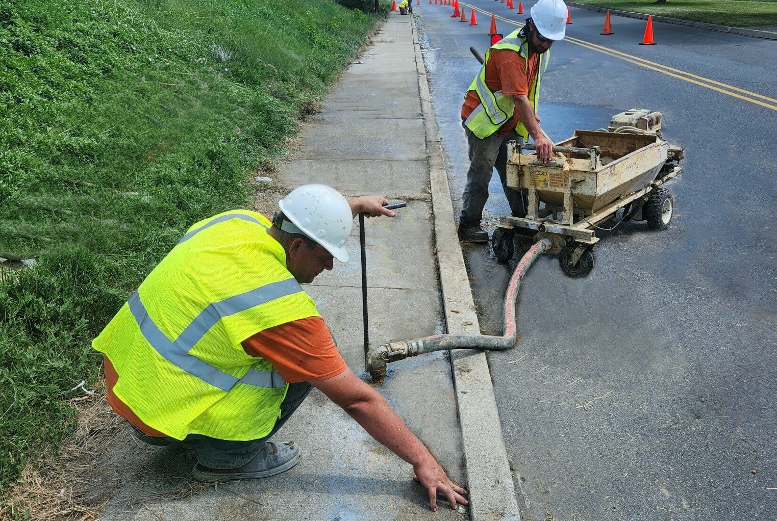 Contractor using a walk-behind concrete grinder to smooth a raised sidewalk joint outdoors with dust control